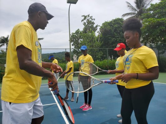 Sandals South Coast Tennis Pro, Normal Hall gets participants in the resort’s Youth Tennis Clinic familiarized with their tennis racquets.