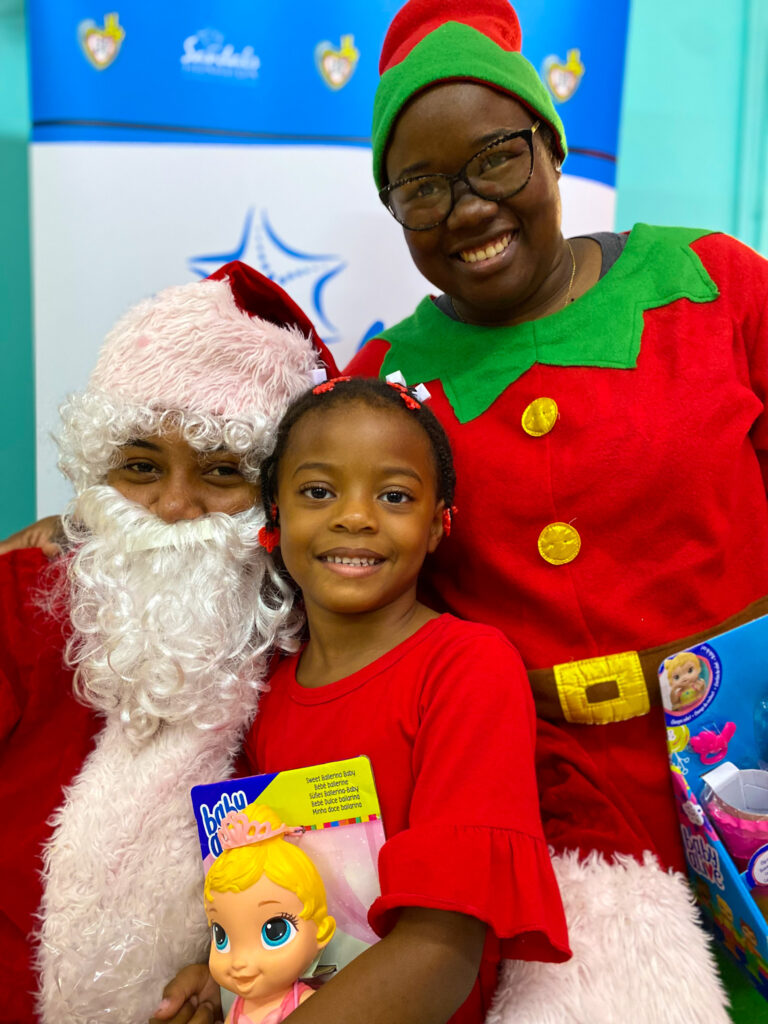 Lucea Infant School student, Azaria Senior (center) was ecstatic to receive her doll for Sandals Negril elf, Kedesha Spence (right) and Santa Claus.