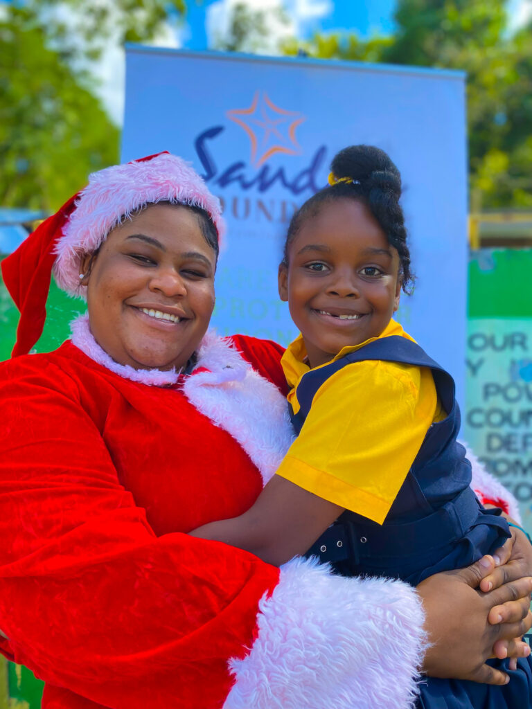 Green Island Primary School student, Shavanique Brown (right) shared hug with Brittney Dewar Sandal Negril’s very own Mrs. Claus for the day. As the Sandals Foundation ambassadors from Sandals and Beaches Negril welcomed the Christmas season with the student body.