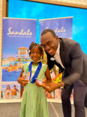 Assistant Learning and Development Manager at Sandals South Coast, Tevin Simpson awards a beaming Abbigale Perry of Petersville Basic School with the second place prize for the Letter Sound and Identification Competition.